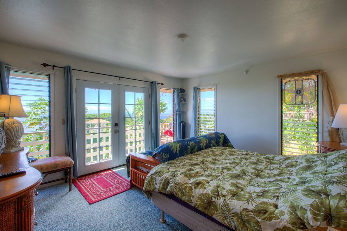 A bedroom with a bed, a desk, a chair, and a window with a view of buildings and greenery.