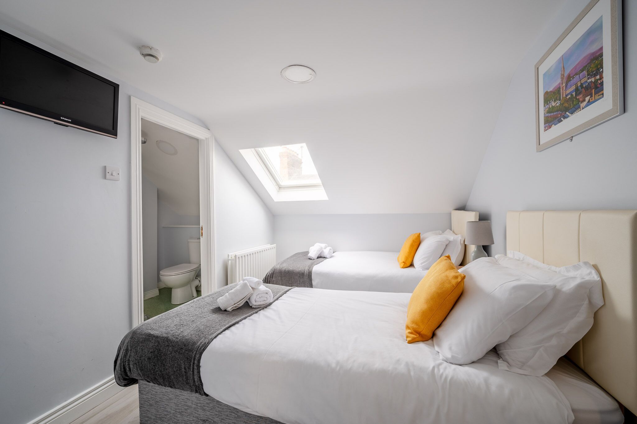 Quarto de hotel com duas camas, um claraboia, uma televisão e um quadro na parede.