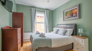 A bedroom with a bed, a dresser, a nightstand, a lamp, and a painting on the wall.