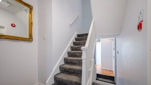 A staircase with carpeted steps and white railings, leading to a door at the bottom.
