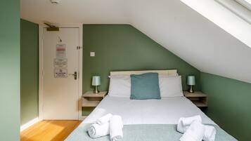 A bedroom with a sloped ceiling, a bed with white linens, two bedside tables with lamps, and a door with a no smoking sign.