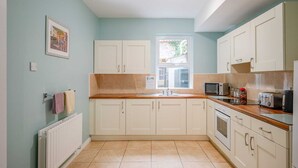 A kitchen with white cabinets, a wooden countertop, a window, and a microwave.