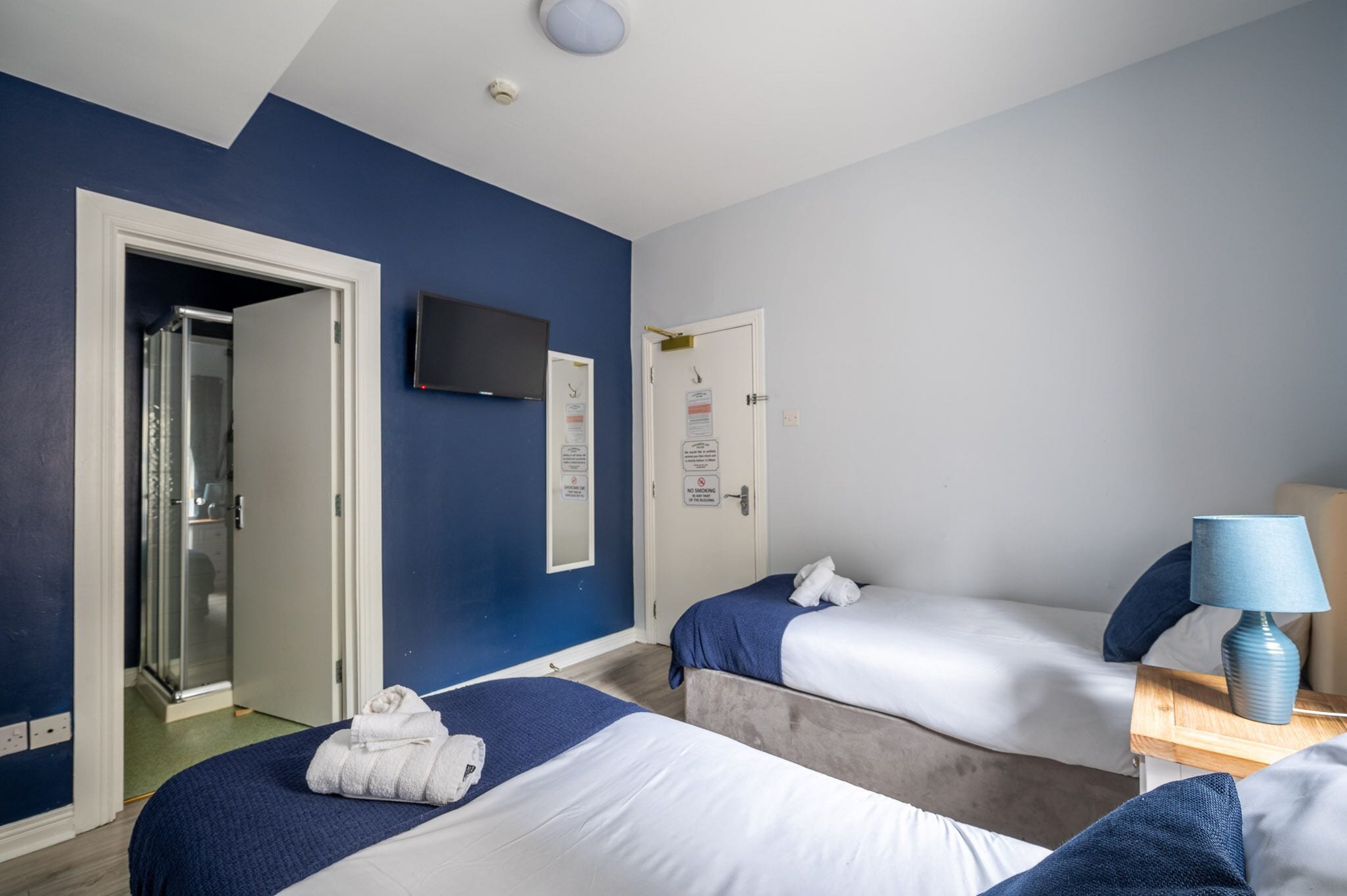 A hotel room with two beds, a shower, a TV, and a lamp.