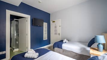 A hotel room with two beds, a shower, a TV, and a lamp.
