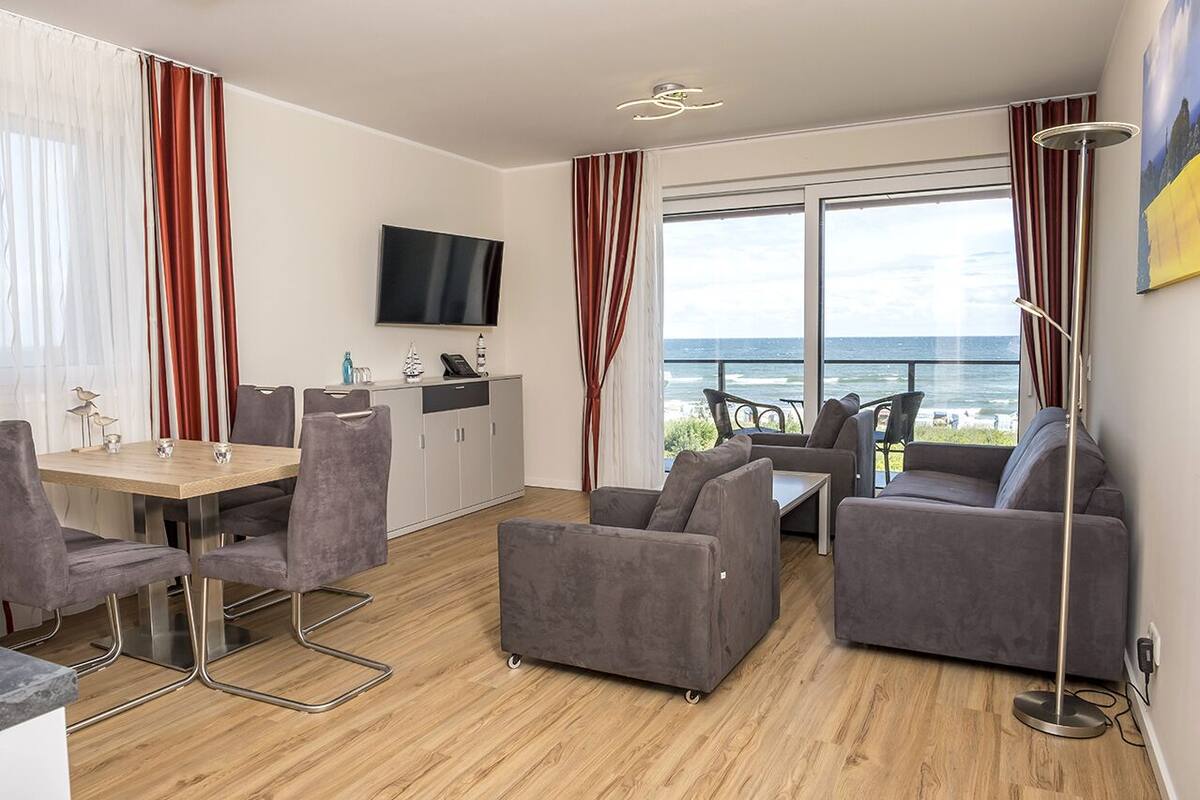 Een moderne woonkamer met een eethoek, grijze banken, een flatscreen-tv en uitzicht op de oceaan.