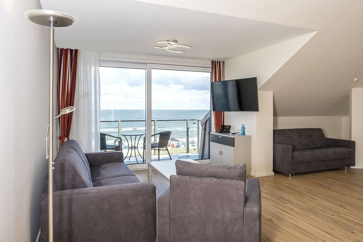 Een moderne woonkamer met een bank, een flatscreen televisie en een balkon met uitzicht op zee.