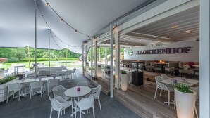 An outdoor patio area with white wicker furniture, a covered seating area, and a view of a garden.