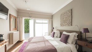 A bedroom with a large bed, a nightstand, a lamp, and a view of the outdoors.