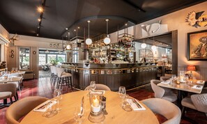 Un restaurant doté d’un bar, de tables rondes décorées de bougies et offrant une vue sur l’extérieur.