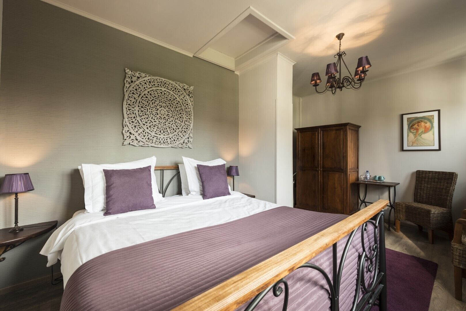 A bedroom with a bed, a wooden bench, a wardrobe, a chair, a table, and a chandelier.