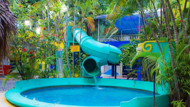 A water slide leading into a pool surrounded by lush greenery. - Posada Real (Rincón de Guayabitos)