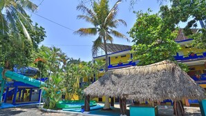 A tropical resort with a thatched-roof hut, palm trees, and a blue and yellow building. - Posada Real (Rincón de Guayabitos)