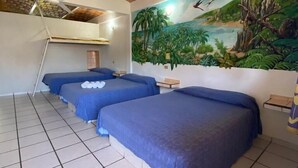 A room with three beds, a mural of a tropical scene, and a sloped ceiling. - Posada Real (Rincón de Guayabitos)