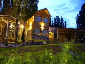 A two-story house with a stone facade, a wooden deck, and a well-lit outdoor area. - Monte Coiron (Malargüe)