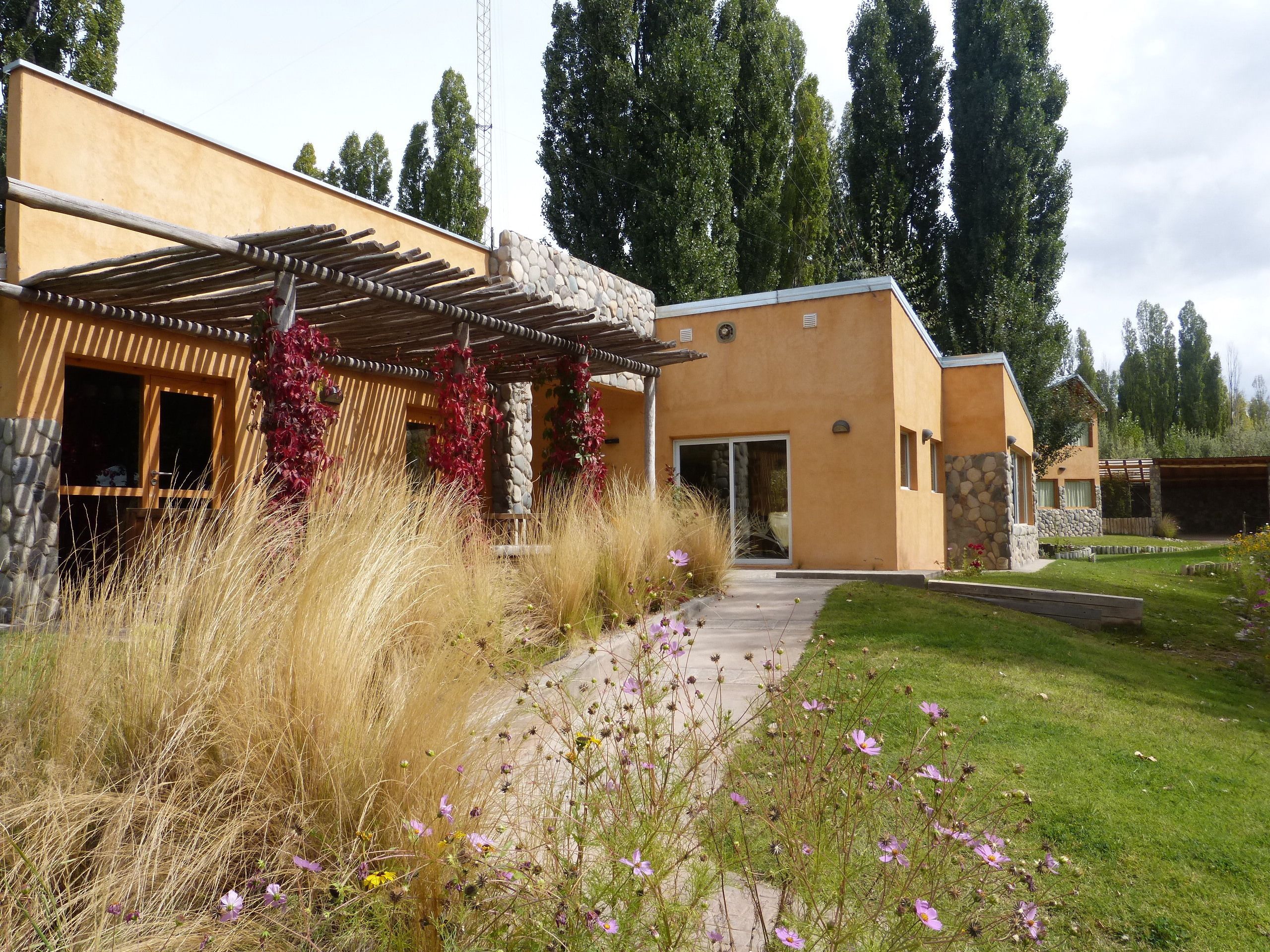 Een modern huis met een stenen gevel, een houten pergola en een pad dat naar de ingang leidt.