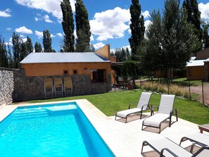 A swimming pool with lounge chairs, a stone wall, and a house with a metal roof. - Monte Coiron (Malargüe)