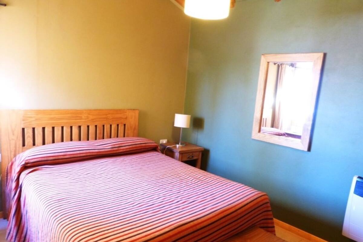 A bedroom with a wooden headboard, a bedside table with a lamp, and a wall-mounted mirror.