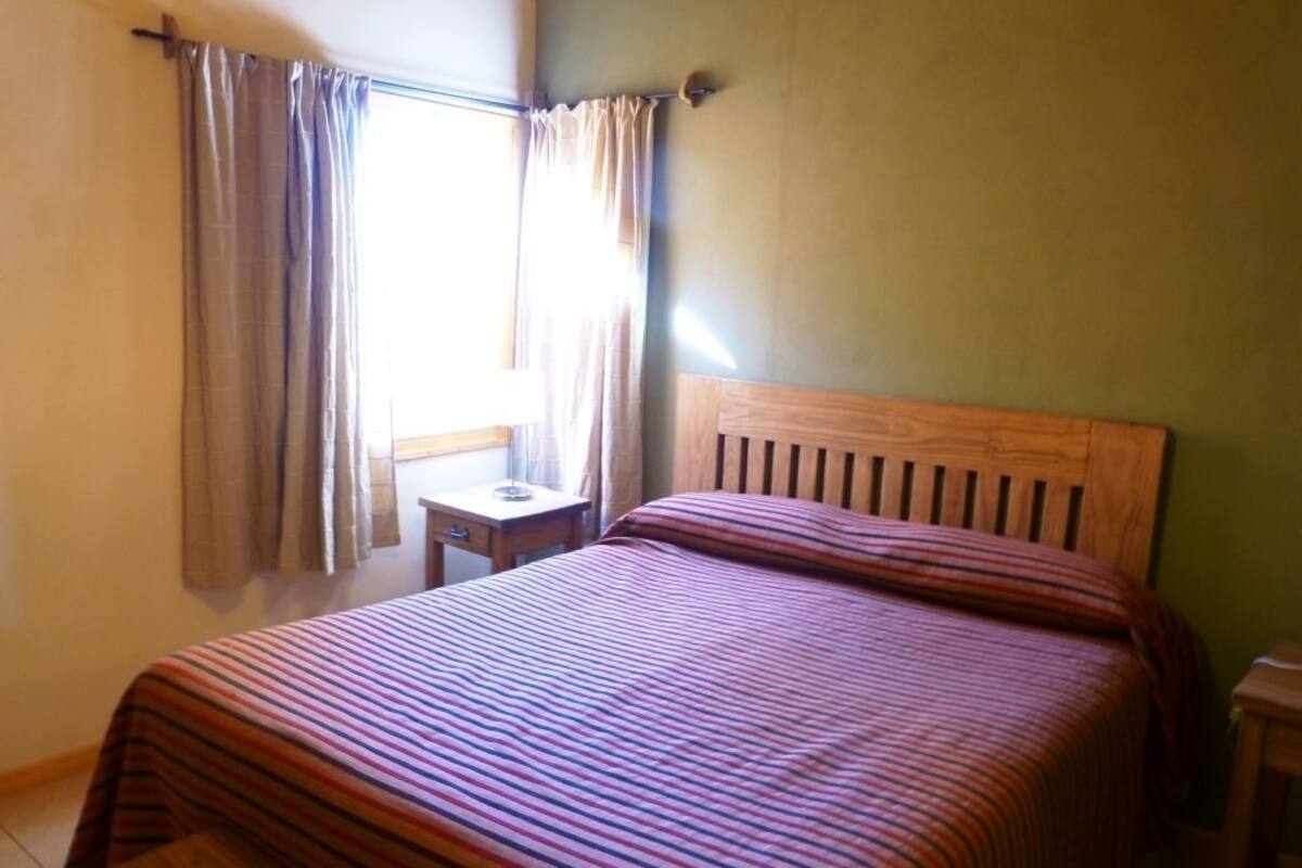 A bedroom with a wooden bed, a small bedside table, and a window with curtains.