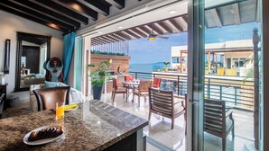 A modern kitchen with granite countertops, a dining area with wooden chairs, and a view of the ocean. - Pinnacle Resorts 180 (Puerto Vallarta)