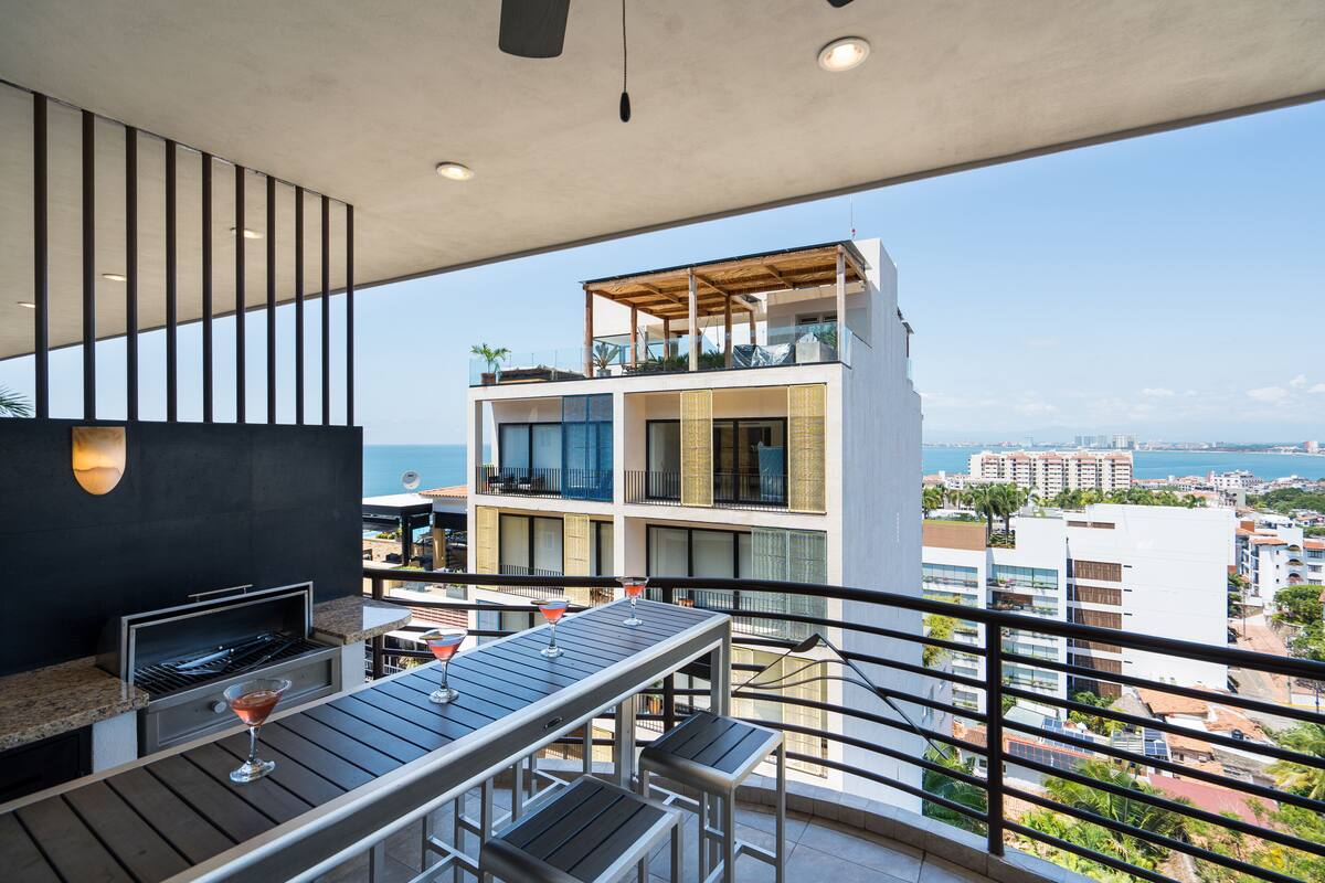 A balcony with a grill, bar area, and a view of the city and sea.