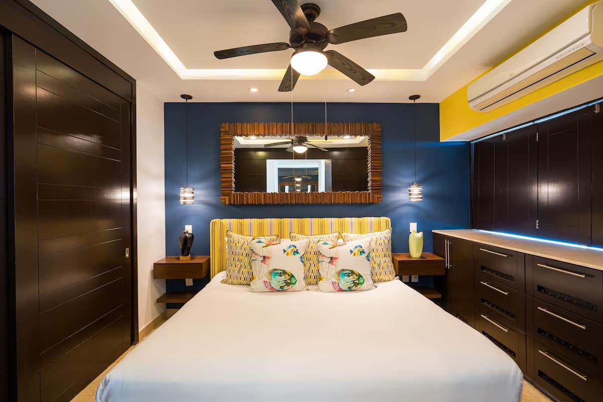 A bedroom with a bed, a ceiling fan, a mirror, and a wardrobe.