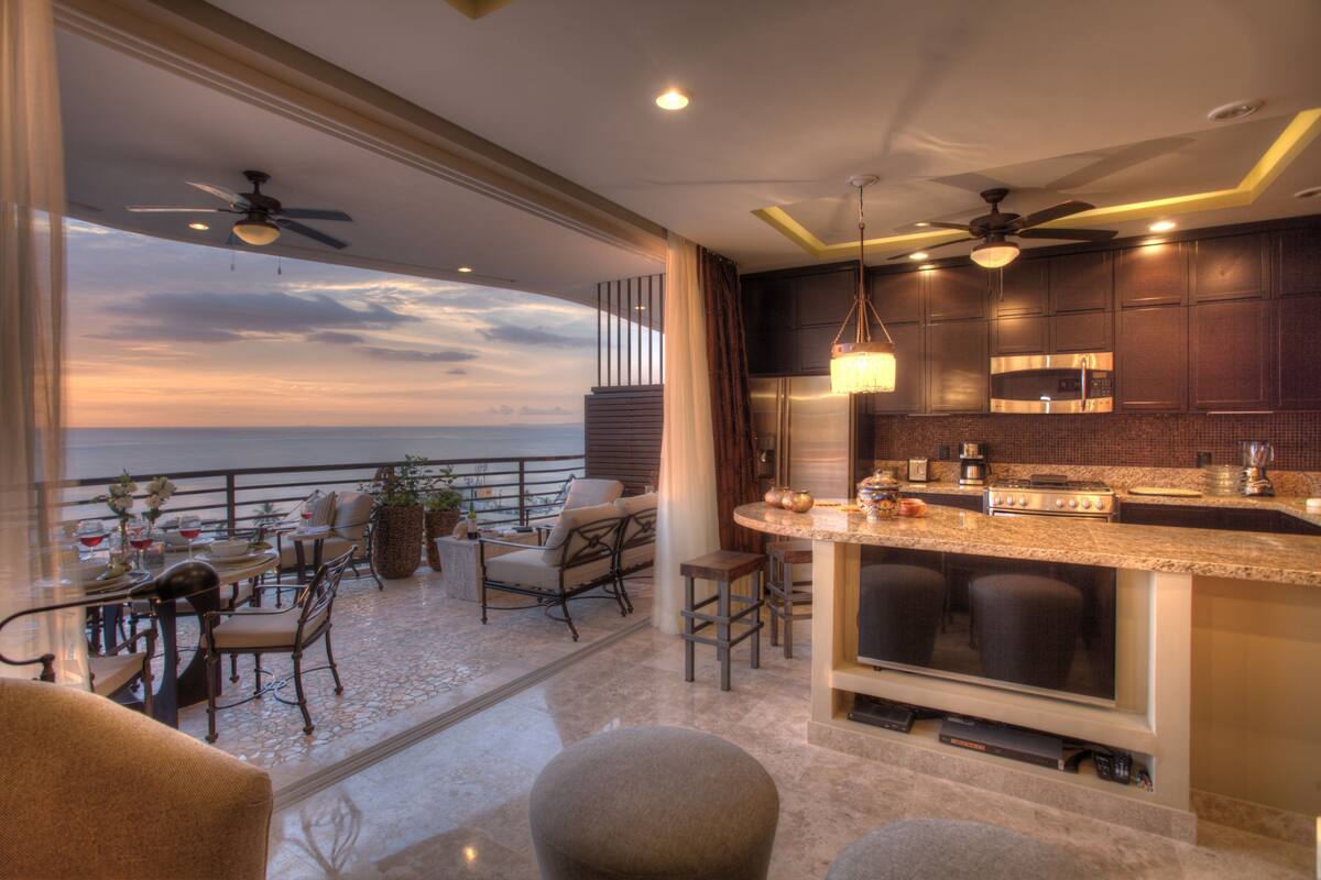 A modern kitchen with a bar area, a dining space with outdoor seating, and a view of the ocean.