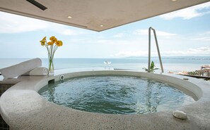 A hot tub with a view of the sea, a vase with flowers, and a towel.