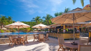 A poolside area with tables and chairs, umbrellas, and a bar. - Infinity Bay Spa & Beach Resort (Roatan)