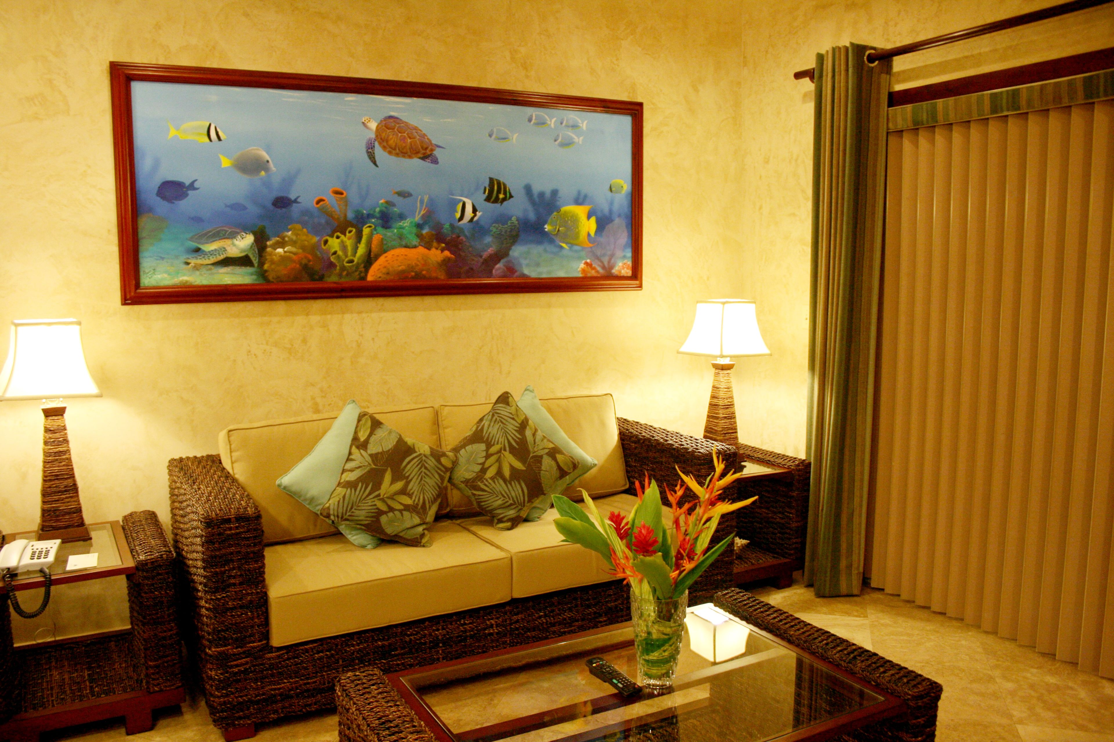 Una sala de estar con un sofá color beige, dos mesitas de noche con lámparas, una mesa de centro y un mural enmarcado con motivos marinos en la pared.