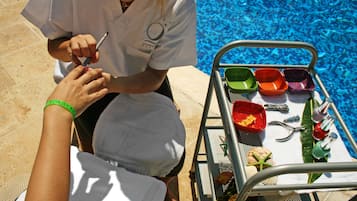Uma pessoa recebendo uma manicure de um profissional perto de uma piscina, com um carrinho de metal contendo diversos objetos.