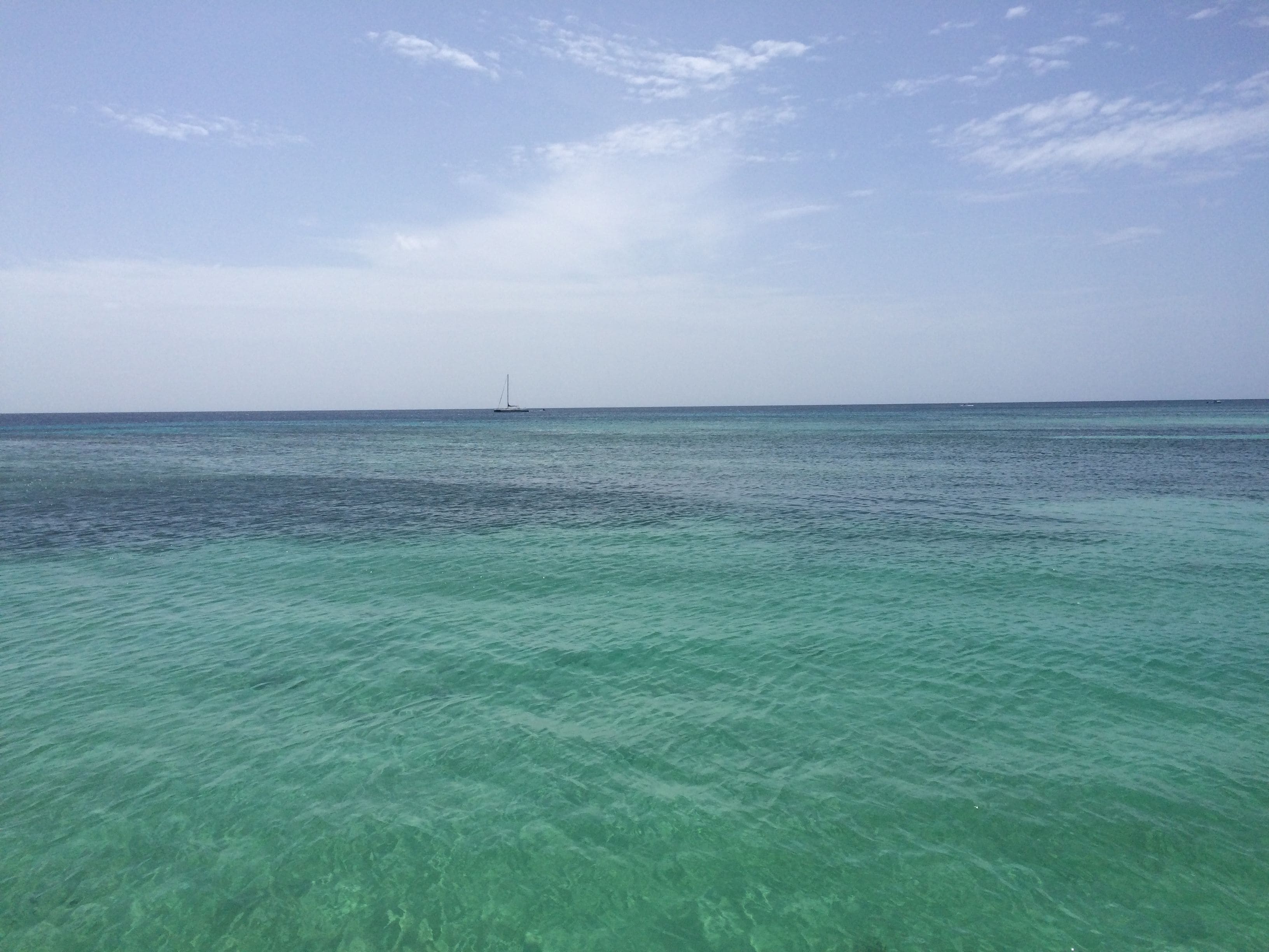 A clear view of a calm sea with a sailboat in the distance.