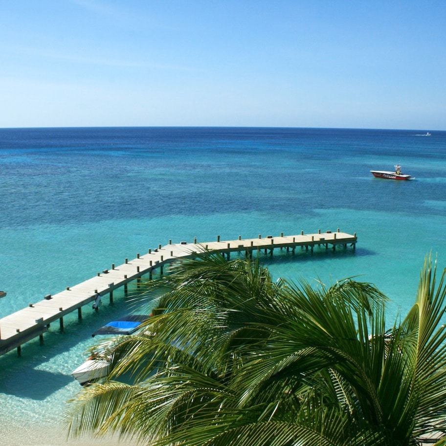 A pier extending into turquoise waters, a boat docked at the end, and a small structure on the left.