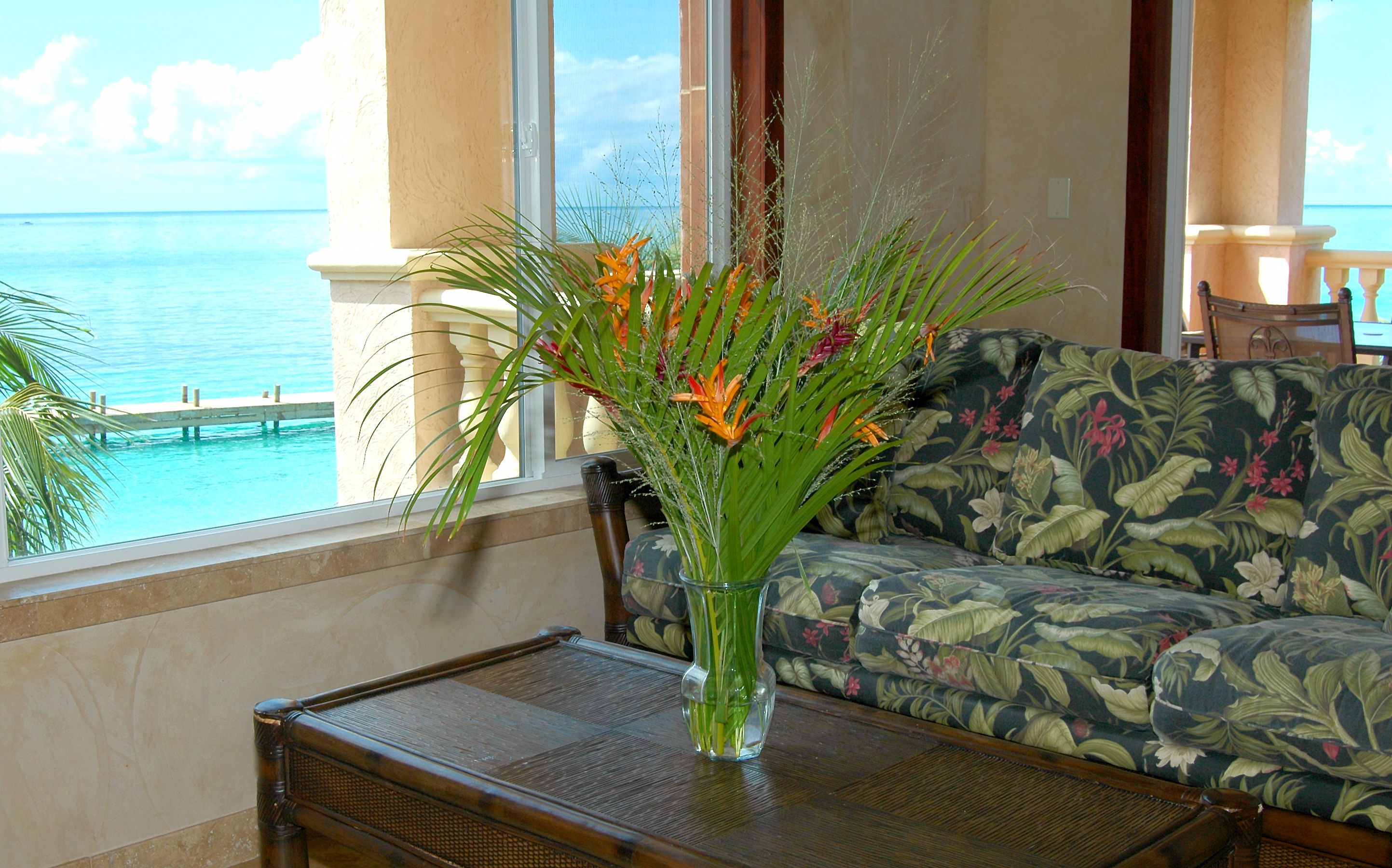 A room with a view of the ocean, a floral sofa, and a vase with flowers on a table.