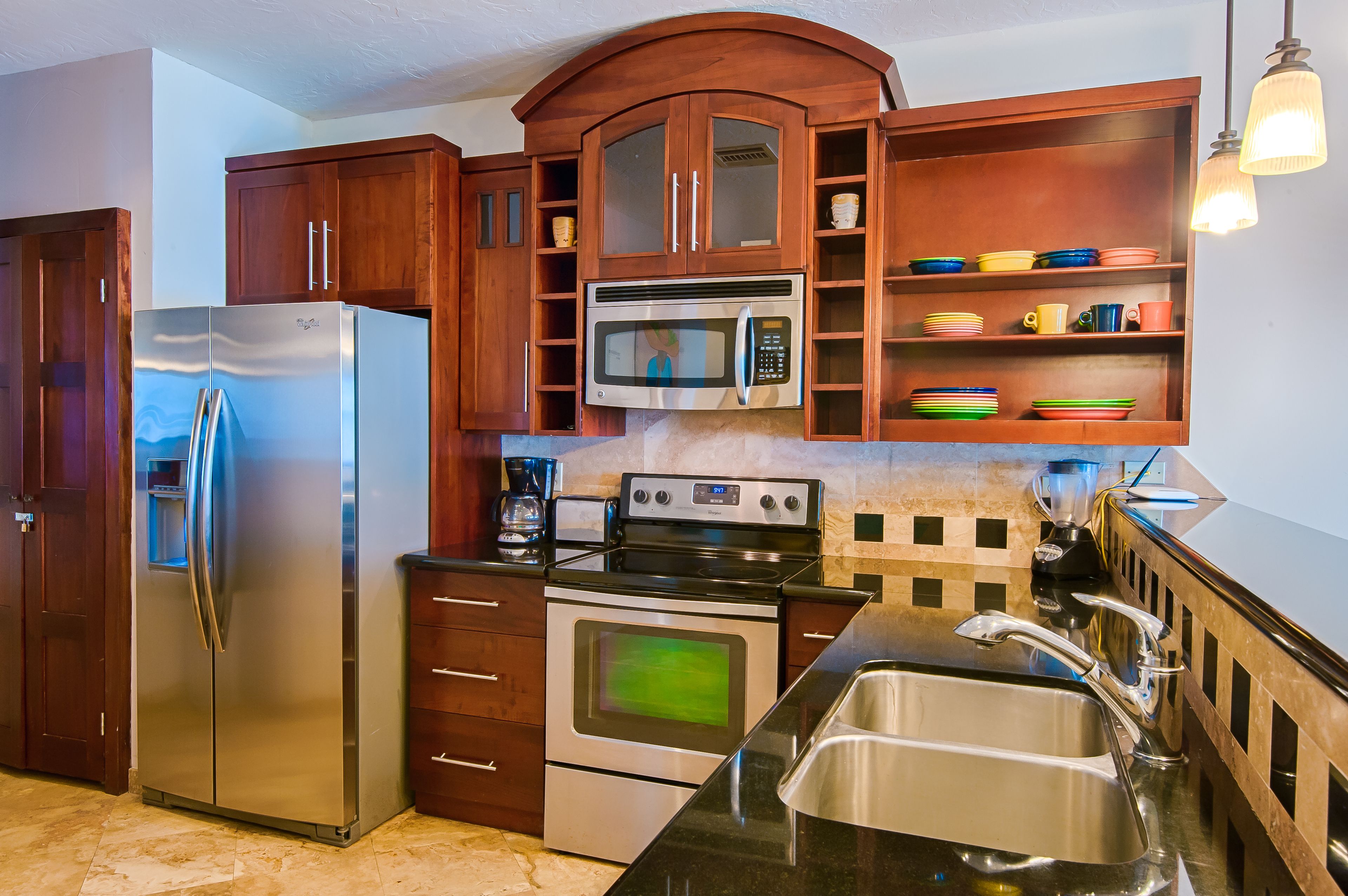 A kitchen with wooden cabinets, a stainless steel refrigerator, a microwave, an oven, and a sink.
