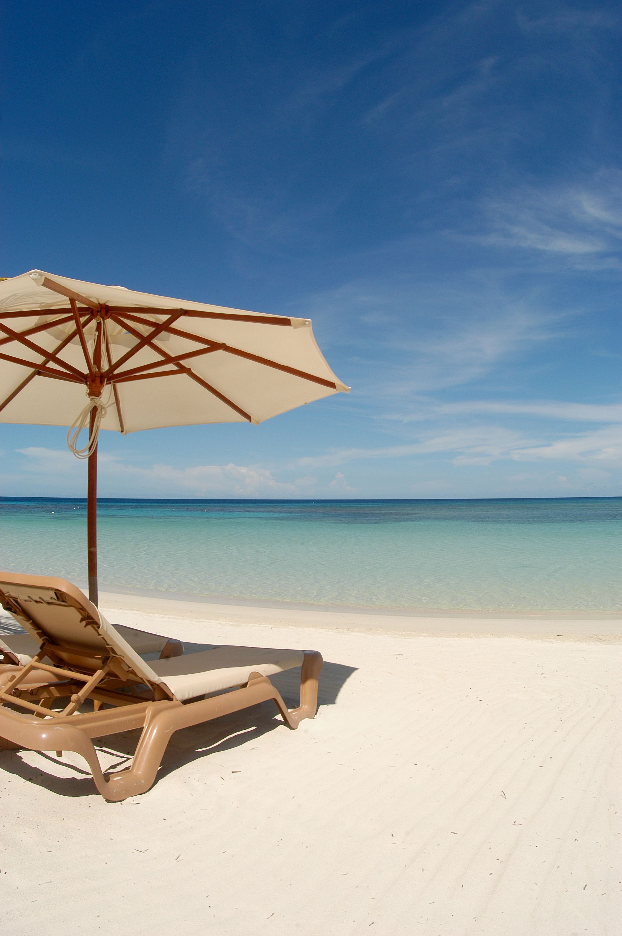 Une scène de plage avec un ciel bleu dégagé, une plage de sable et une chaise longue placée sous un parasol.