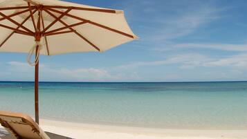 Une scène de plage avec un ciel bleu dégagé, une plage de sable et une chaise longue placée sous un parasol.