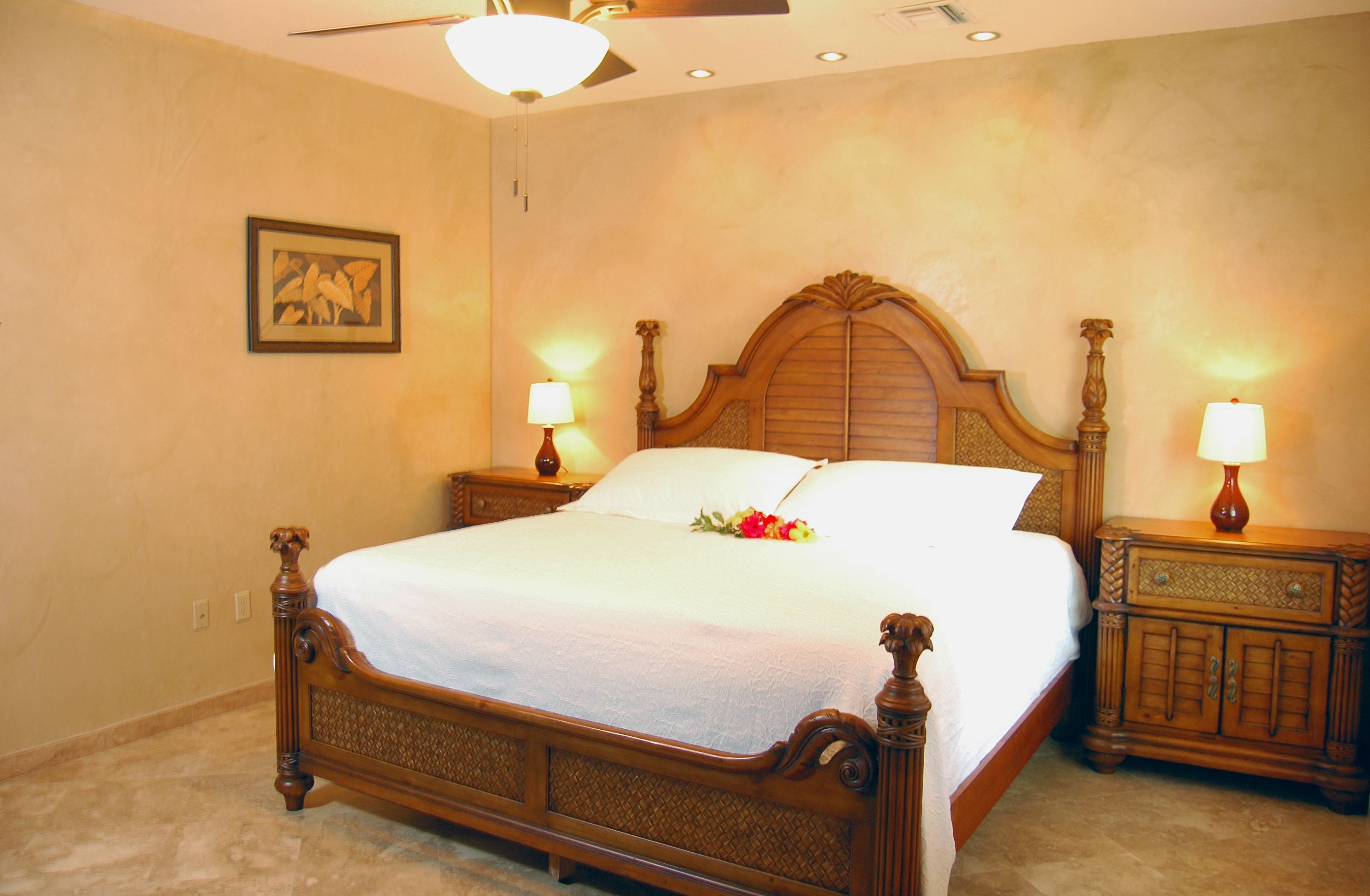 A neatly made bed with a wooden headboard, two bedside tables with lamps, and a framed picture on the wall.