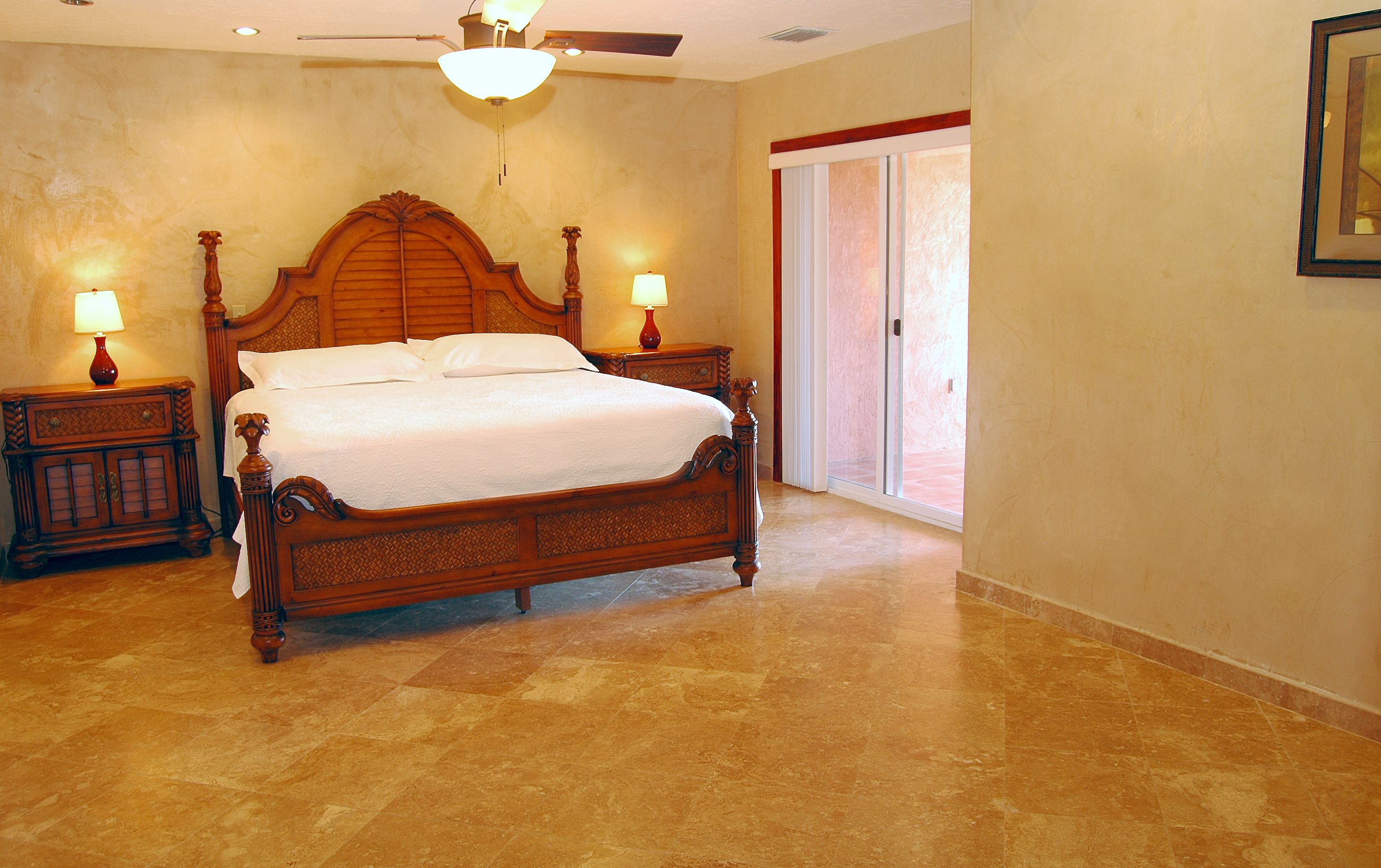 A bedroom with a wooden bed, two nightstands with lamps, a ceiling fan, and a large window.