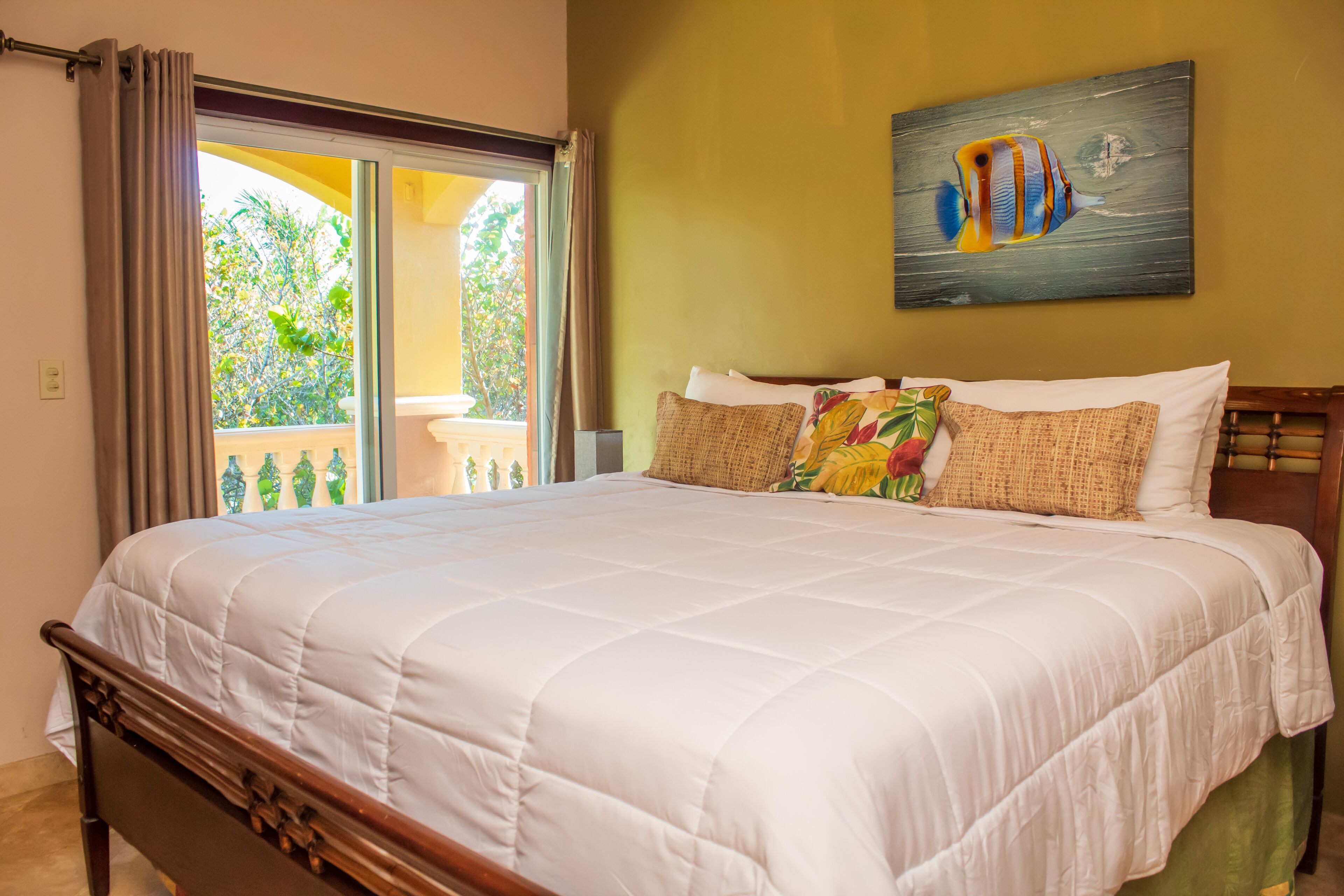 Un dormitorio con una cama grande, una ventana con cortinas, un cuadro de un pez y vistas a zonas verdes al exterior.