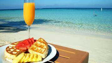 A plate with waffles, watermelon, and pineapple on a beach with clear water and a clear sky.