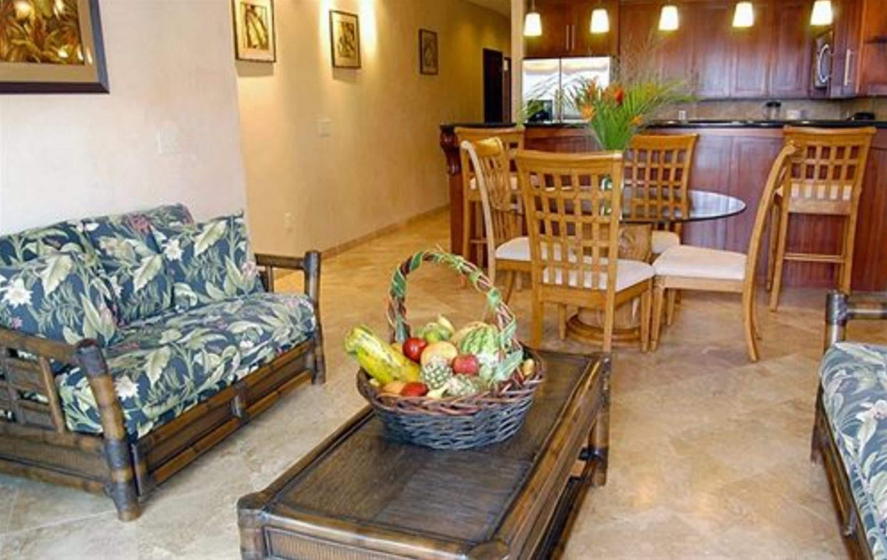 Una sala de estar con un sofá, sillas, una mesa de centro y una cesta de frutas.