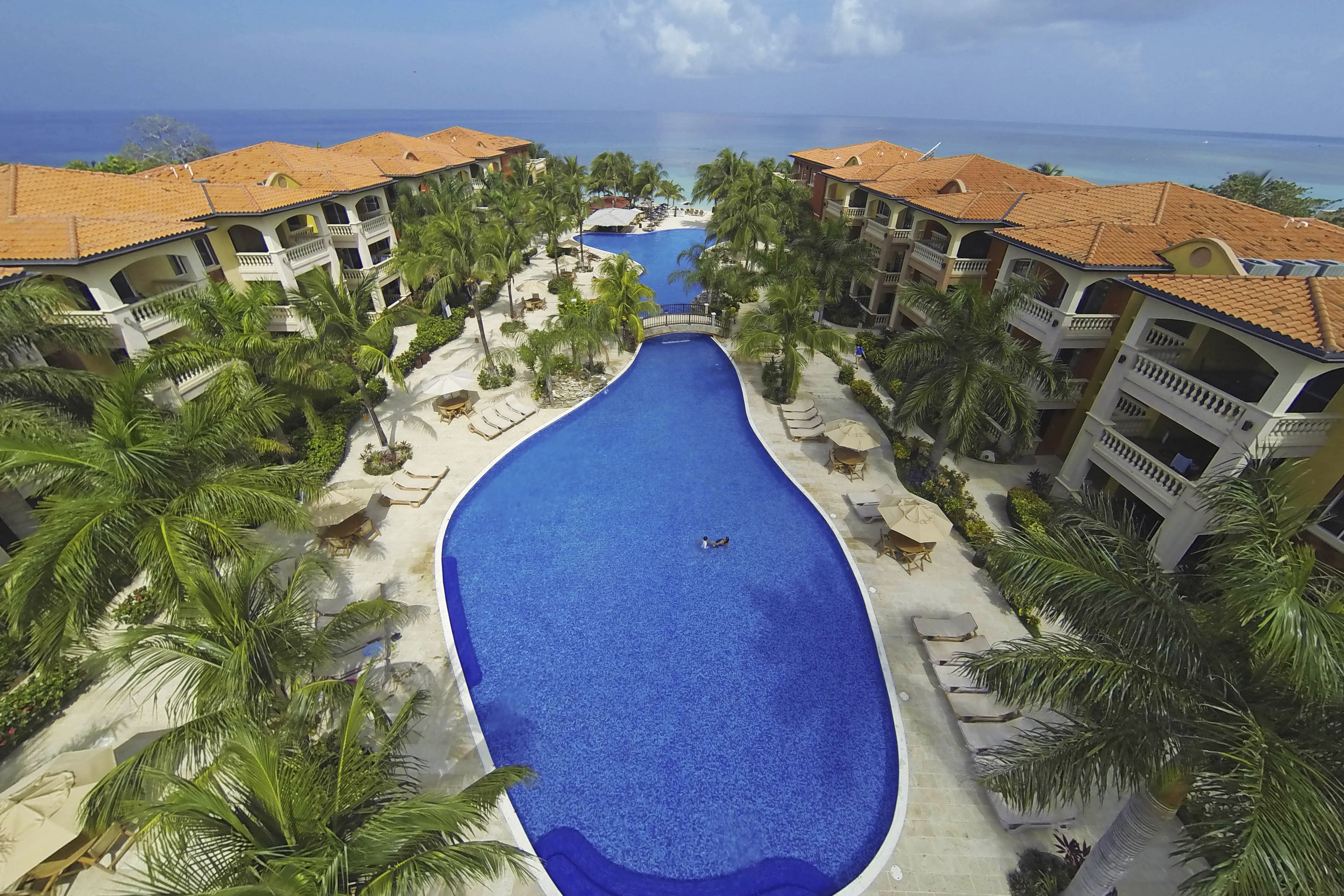 Un resort con piscina central, palmeras y vistas al océano.