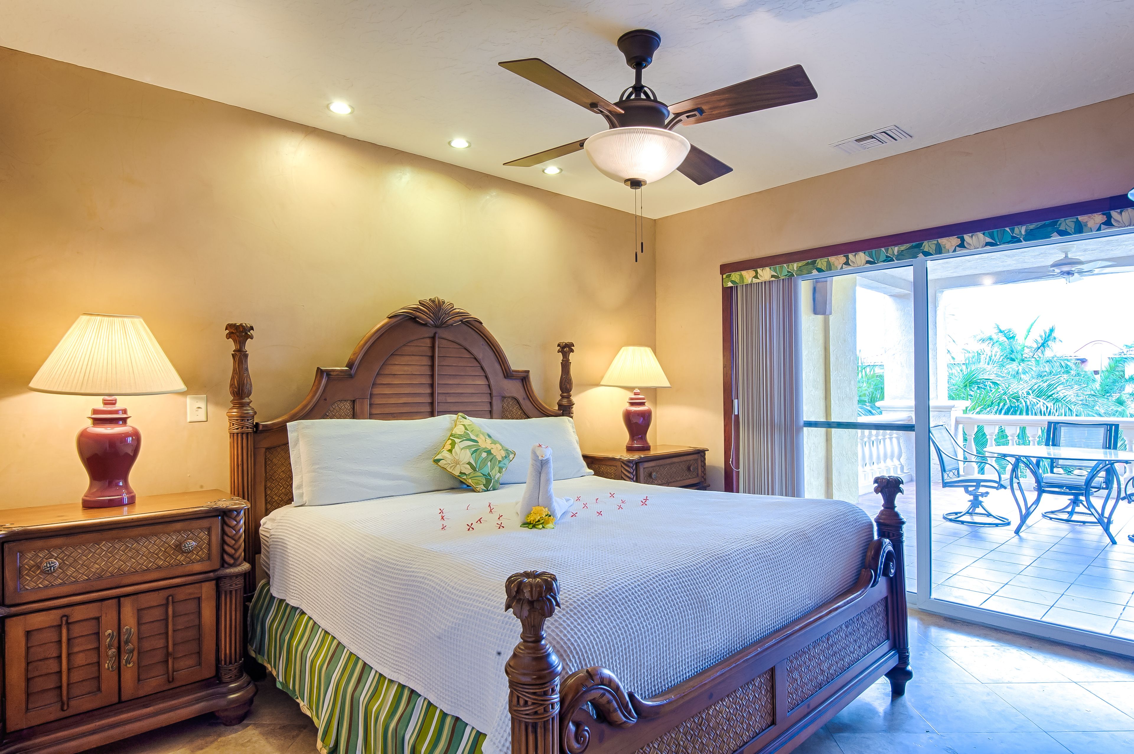 A hotel room with a large bed, wooden headboard, two bedside lamps, and a ceiling fan.