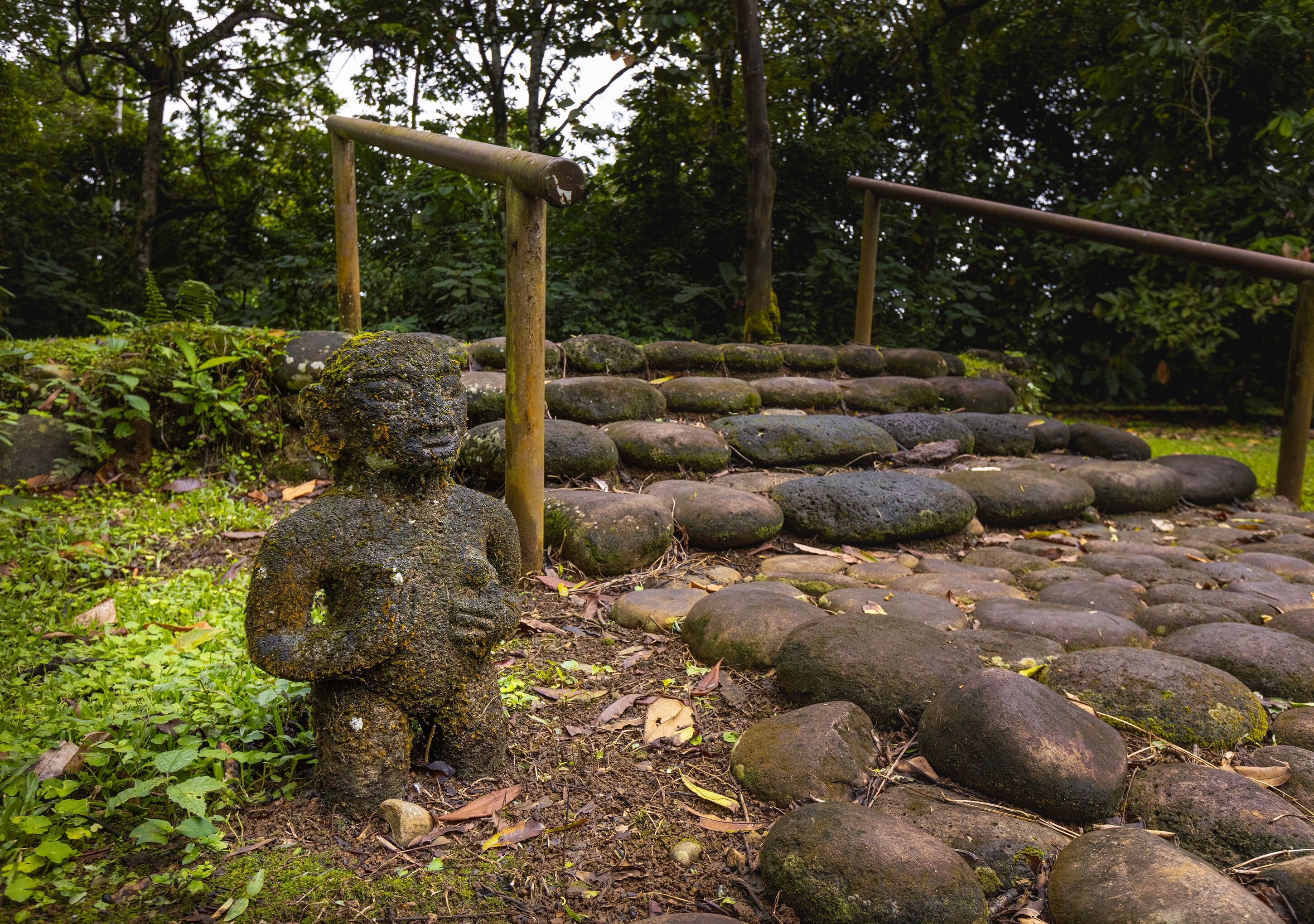 A stone statue in a forested area with a series of stone steps leading up to it.