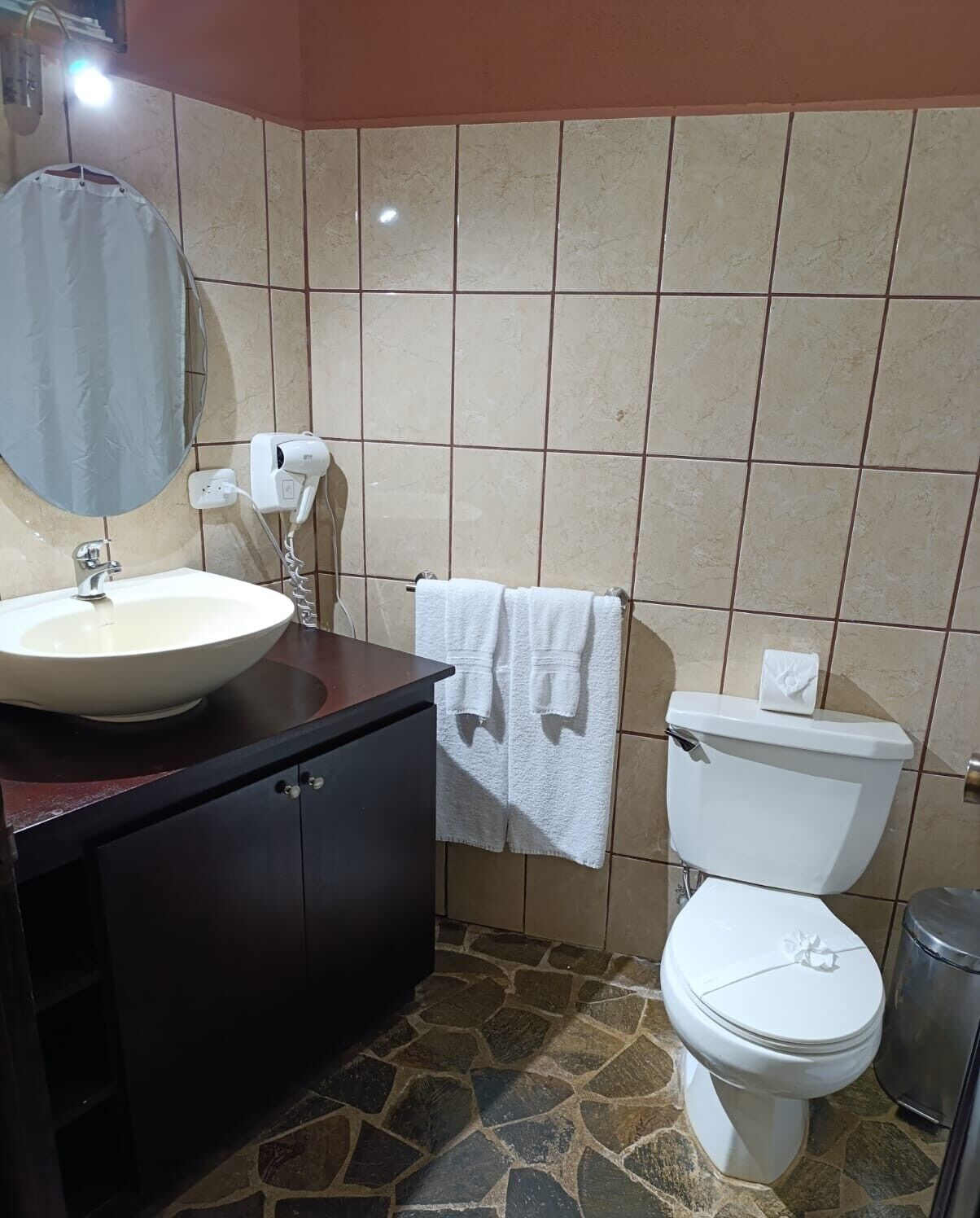 A bathroom with a sink, mirror, towel rack, toilet, and a trash bin.