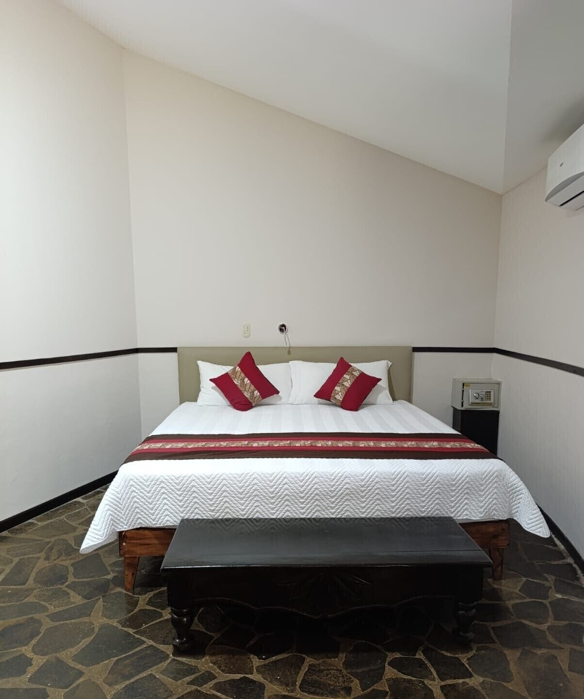A bedroom with a bed, a bench, a nightstand, and an air conditioning unit.