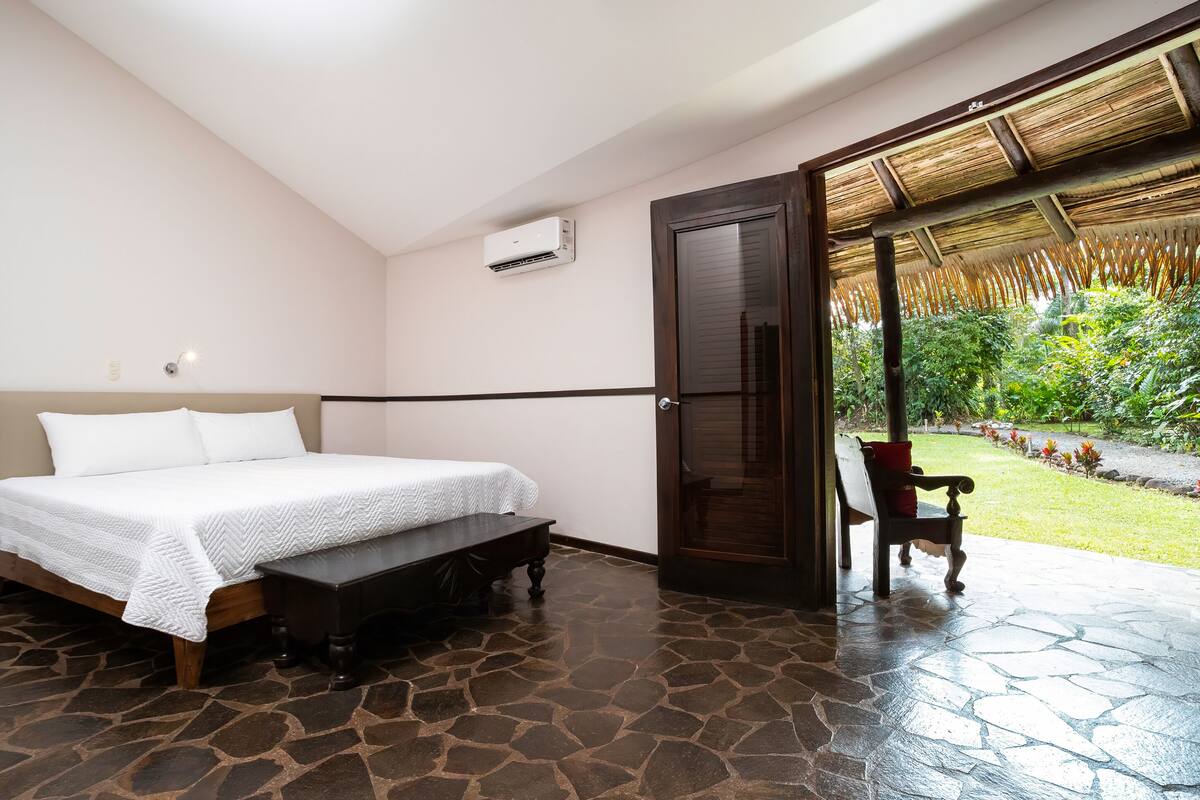 Een slaapkamer met een bed, een bankje, een deur naar een balkon en een airconditioning.