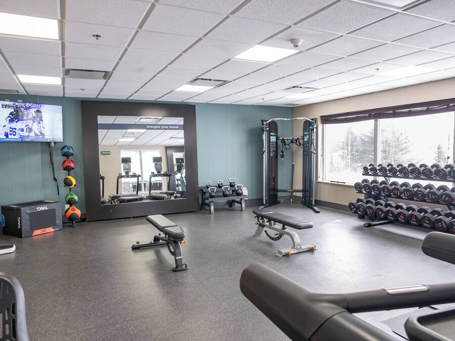 A gym with exercise equipment, a mirror, a TV displaying a sports game, and a rack of dumbbells.