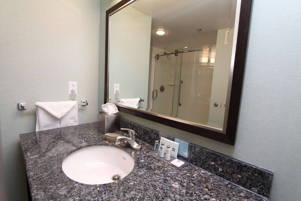 A bathroom with a granite countertop, a white sink, a mirror, and a glass shower enclosure.