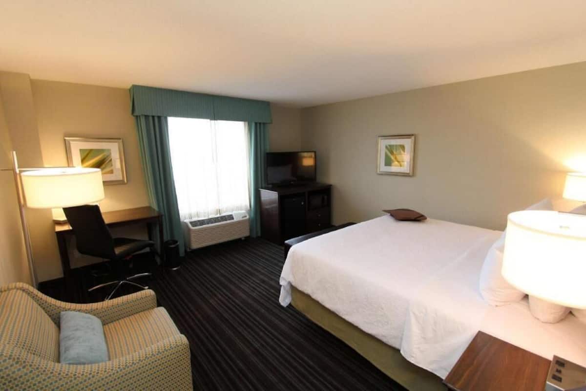 A hotel room with a bed, a desk with a chair, a television, and two wall-mounted lamps.